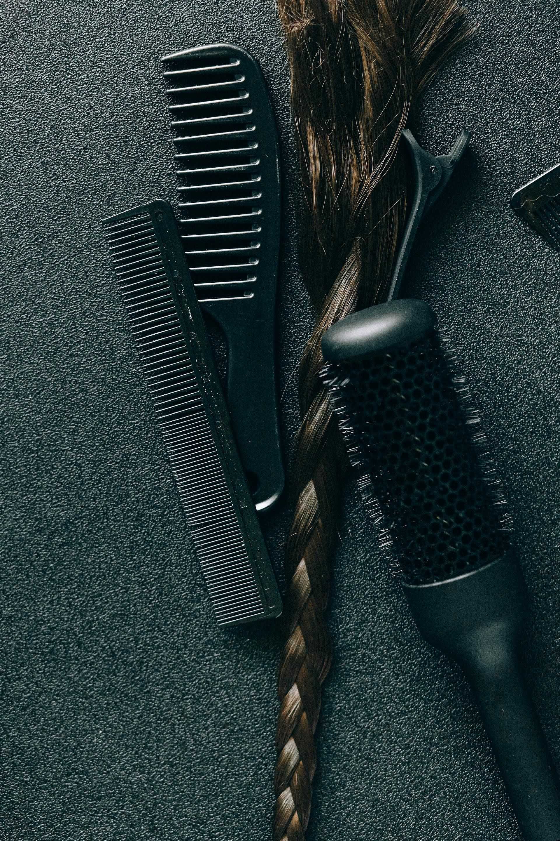 Braided brown hair with black combs and hairbrush on a dark surface.