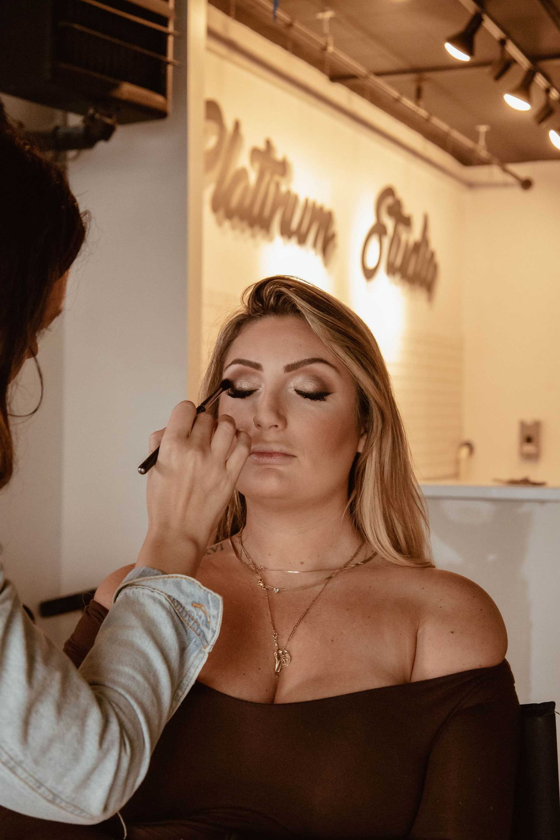 Makeup artist applying eyeshadow to a seated woman in a studio.