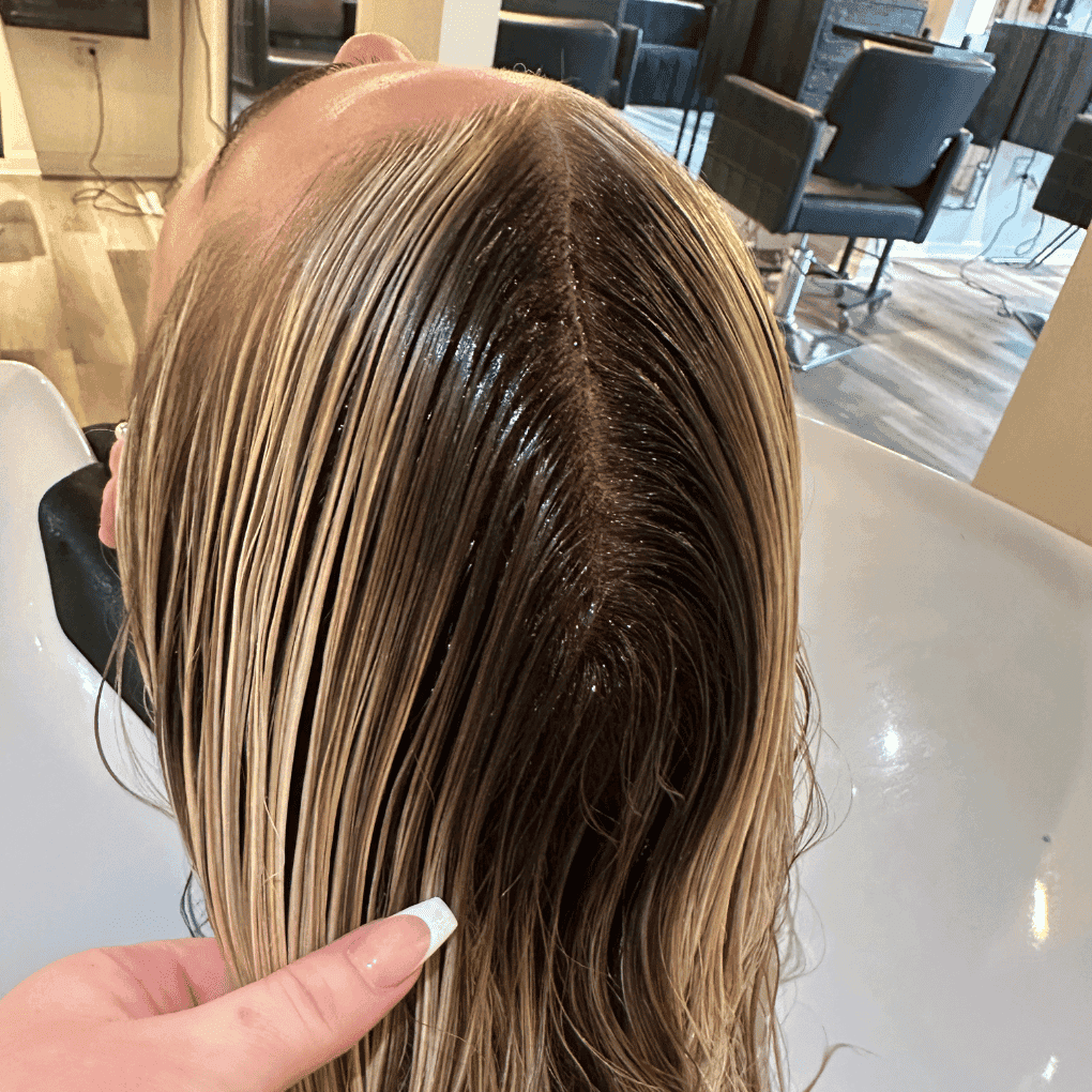 Hair salon client getting hair washed at a sink, stylist's hand holding wet blond hair.