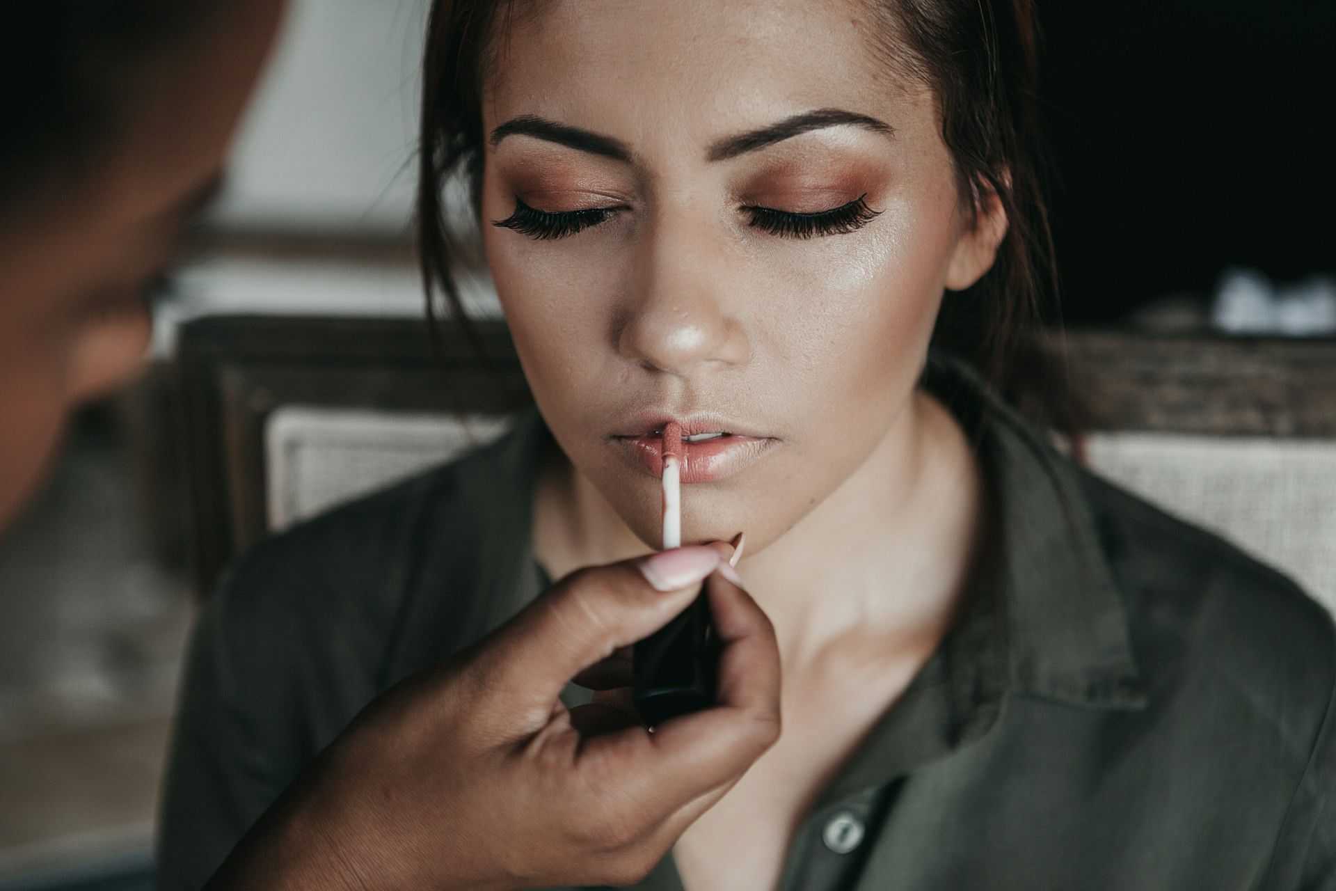 Woman getting makeup applied, focusing on lips, in a calm setting.